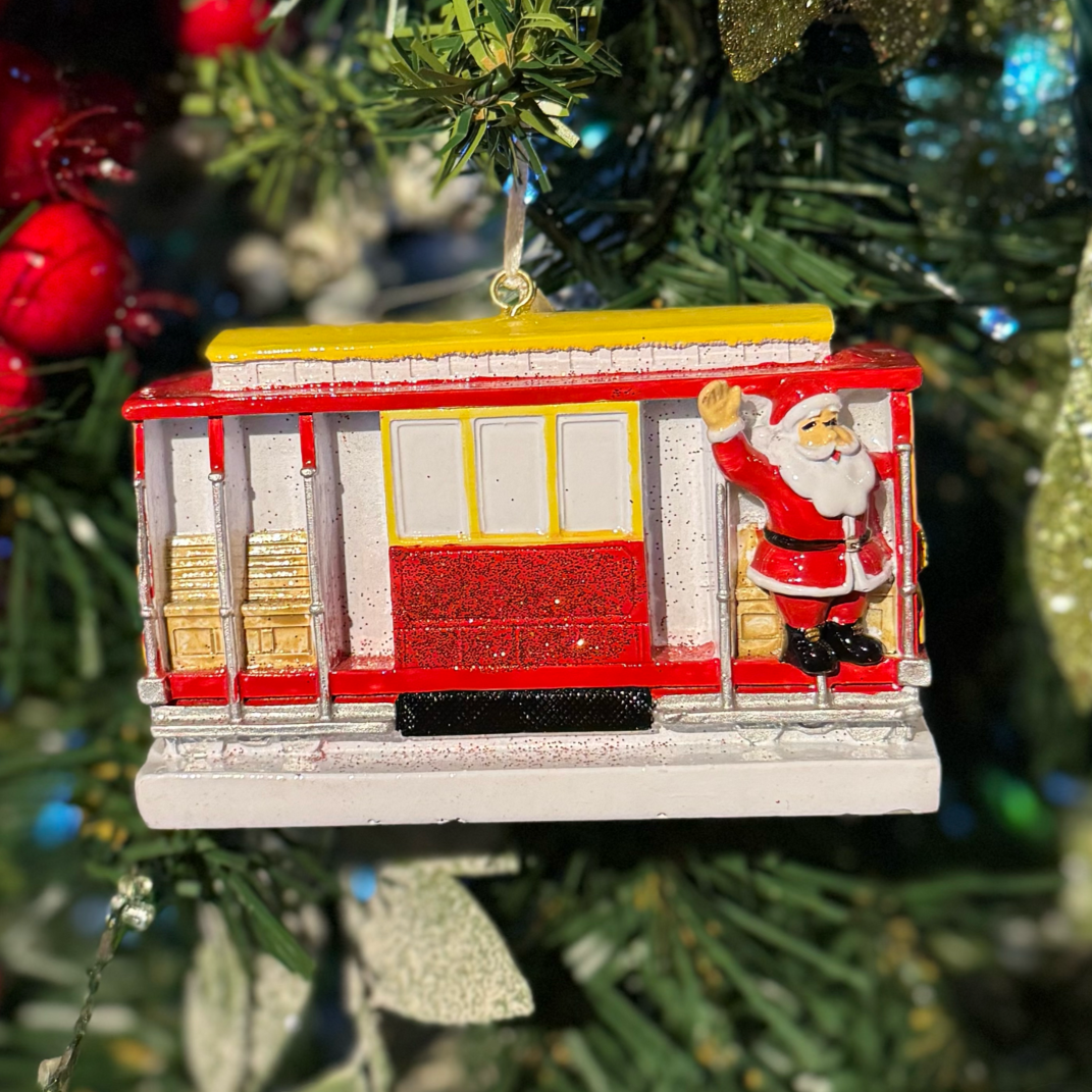 Christmas ornament of a red trolley with Santa Claus on a decorated tree.