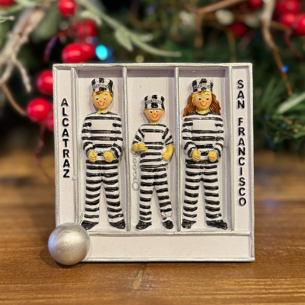 Three figures in striped prison uniforms in a jail cell labeled 'Alcatraz' and 'San Francisco' with a Christmas tree in the background.