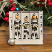 Three figures in striped prison uniforms in a jail cell labeled 'Alcatraz' and 'San Francisco' with a Christmas tree in the background.