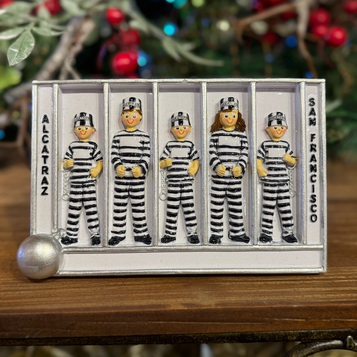 Decorative figurines of prisoners in striped uniforms in a display case with 'Alcatraz' and 'San Francisco' text, against a festive background.